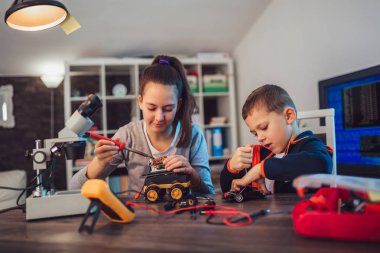 Mutlu gülümseyen erkek ve kız teknik robot oyuncak ve yapmak oluşturur. Tablo ayrıntılarını tam teknik oyuncak