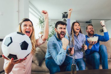 Mutlu arkadaşlar ya da futbol taraftarları televizyonda maç izleyip zaferi evde kutluyorlar. Dostluk, spor ve eğlence kavramı..