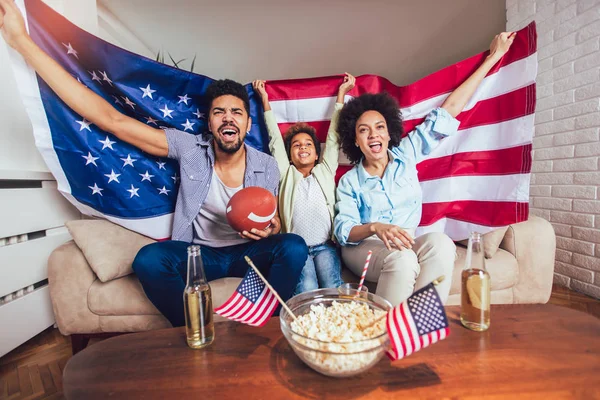 Happy African American family of three watching tv and cheering sport games on sofa at home