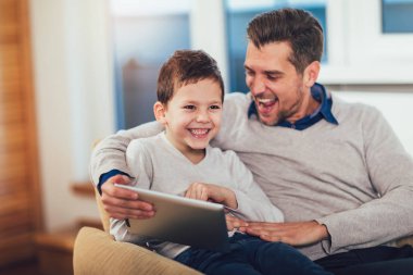 Baba ve oğul evde, bir tablet üzerinde oynarken eğleniyor.