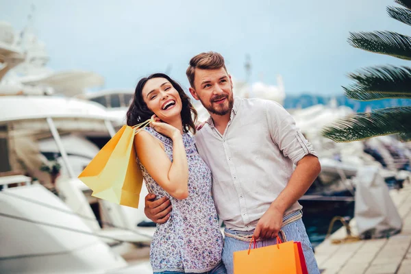 背景にボートで観光シー リゾートの港で歩いて買い物袋を持つ幸せな若いカップル — ストック写真