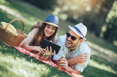 İki meyvelerle dolu bir piknik sepeti ile bir parkta piknik battaniye yatan, onlar dijital tablet kullanıyorsanız