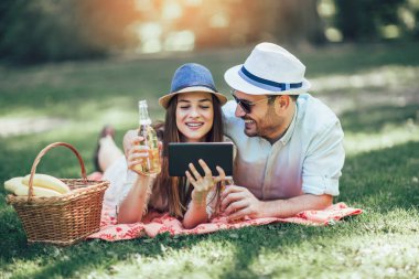 İki meyvelerle dolu bir piknik sepeti ile bir parkta piknik battaniye yatan, onlar dijital tablet kullanıyorsanız