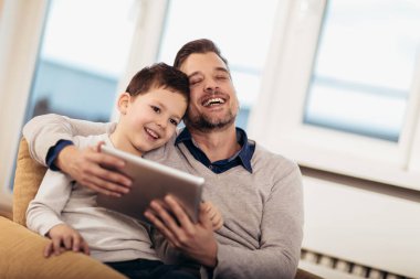 Baba ve oğul evde, bir tablet üzerinde oynarken eğlenceli, seçici odak sahip.