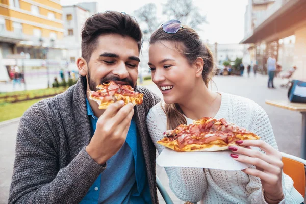 Couple eating pizza outdoors and smiling.They are sharing pizza in a outdoor cafe.