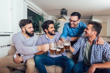 Erkekler televizyonda birlikte spor izleyip neşeli çığlıklar atıyorlar. Bir grup arkadaş kanepede oturup futbol maçı izliyorlar..