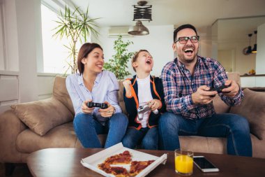Mutlu aile kanepede oturuyor ve video oyunları oynamak ve pizza yemek