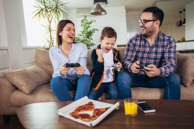 Mutlu aile kanepede oturuyor ve video oyunları oynamak ve pizza yemek