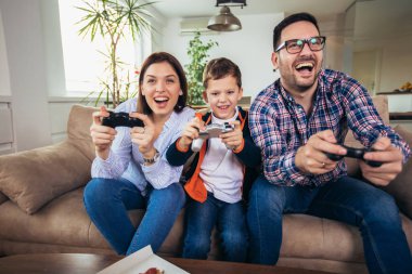Mutlu aile kanepede oturuyor ve video oyunları oynamak ve pizza yemek