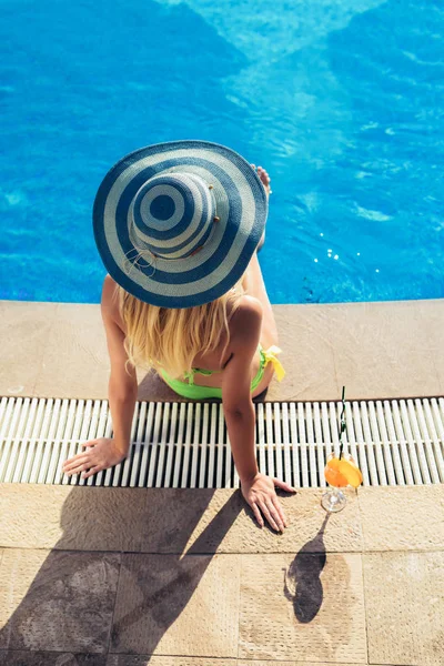 Young woman with cocktail glass chilling in the tropical sun near swimming pool