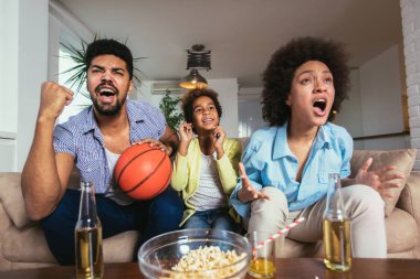 Üç tv izlerken ve spor oyunları evde kanepe üzerinde tezahürat mutlu Afro-Amerikan ailesi