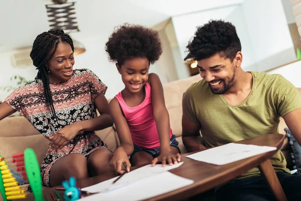 Mom and dad drawing with their daughter. African american family spending time together at home.