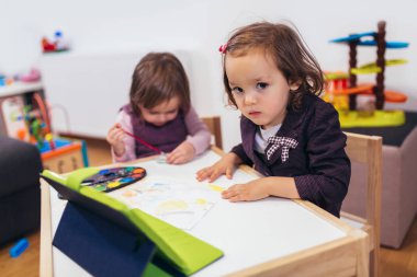 İki sevimli küçük kız bir dijital tablet ile evde oynarken. 