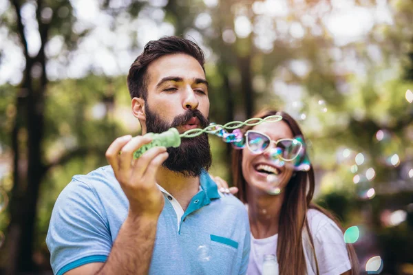 Paar sitzt auf der Parkbank und pustet Suppenblasen auf Bea — Stockfoto