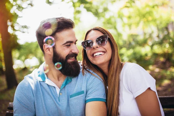 Paar sitzt auf der Parkbank und pustet Suppenblasen auf Bea — Stockfoto