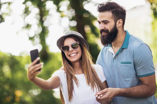 Mladý pár pomocí mobilního telefonu s selfie v parku — Stock fotografie
