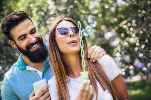 Ζευγάρι, κάθονται στον πάγκο πάρκο και φυσώντας φυσαλίδες σούπα στην bea — Φωτογραφία Αρχείου