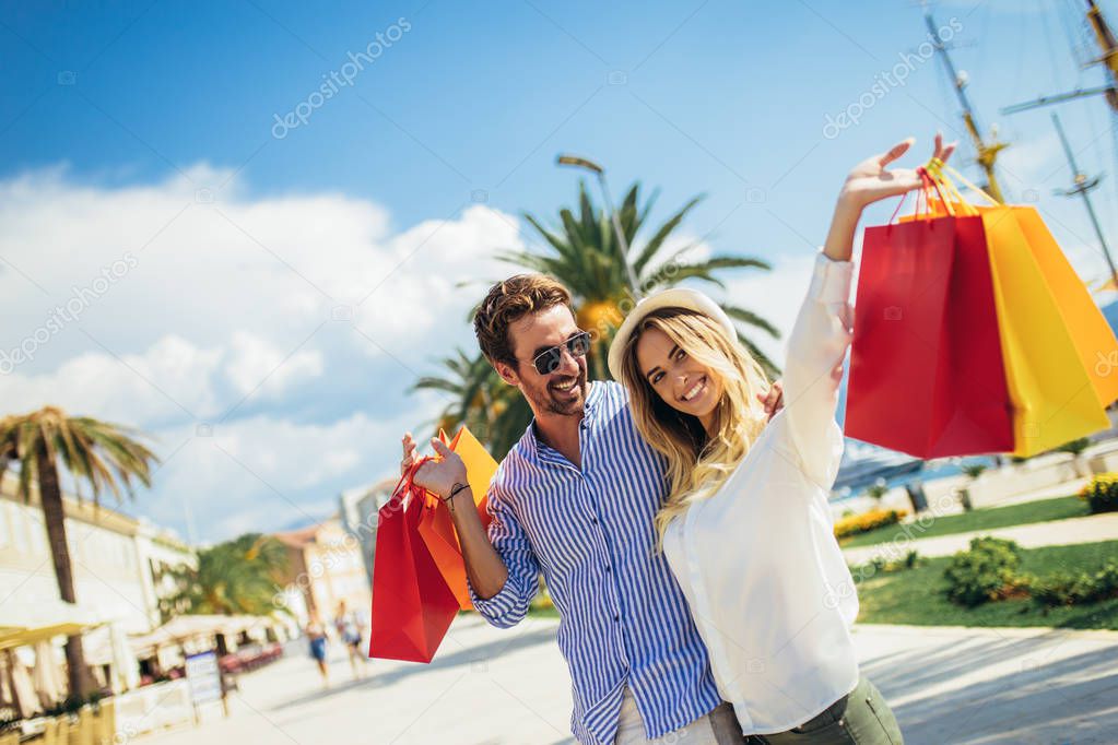 Happy young couple with shopping bags walking by the harbor of a