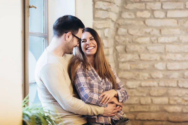 Portrait of a young couple hugging next to the window, brick wal — Stock Photo, Image