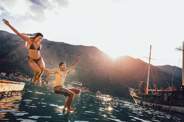 Mladý pár, skoky do vody z mola — Stock fotografie