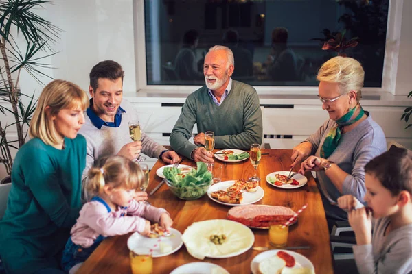 Flergenerasjonsfamilie nyter måltidet rundt bordet hjemme – stockfoto