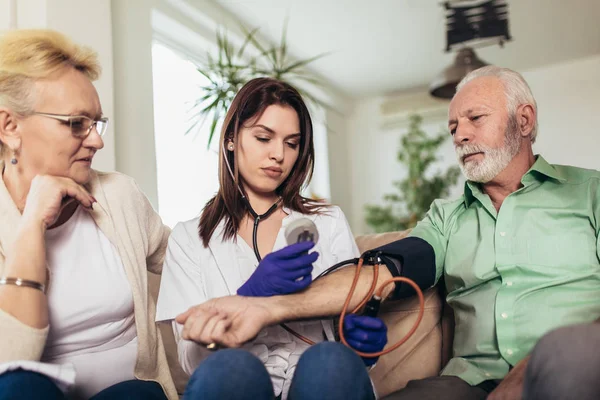 Young medic taking blood pressure during home visit — Stock Photo, Image