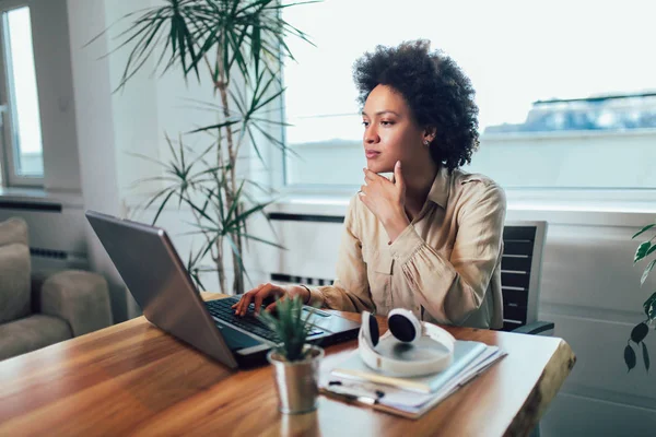 Leende unga afrikanska kvinnliga entreprenör sitter vid ett skrivbord i h — Stockfoto