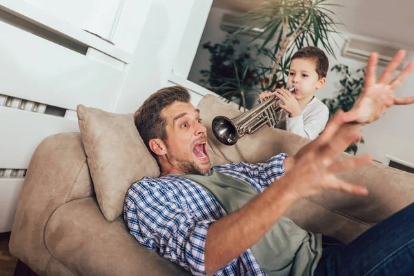 Wakey wakey! Son wakes up his dad by playing a trumpet. — Stock Photo, Image