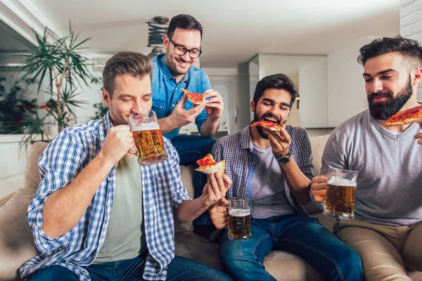 Grupo de cuatro amigos varones que beben cerveza y comen pizza en hom —  Fotos de Stock