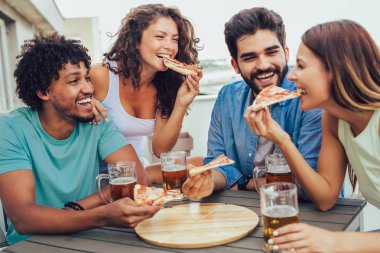 Arkadaşlar pizza nın tadını çıkarıyor. Pi yiyen bir grup genç neşeli insan