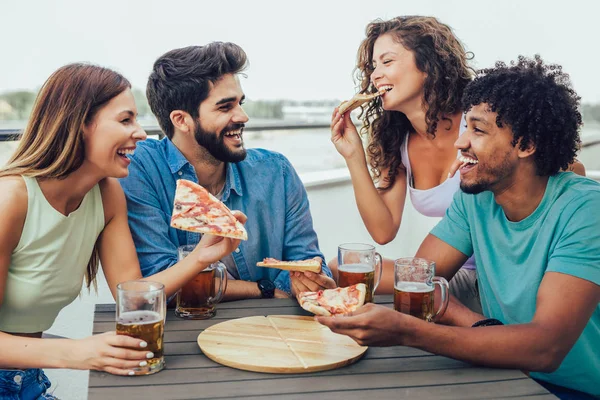 Друзья наслаждаются пиццей. Группа молодых веселых людей, которые едят пи — стоковое фото