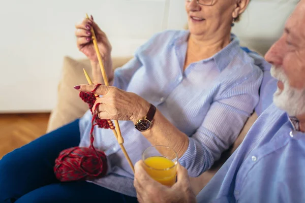 Senior woman teaching her husband the art of knitting woollen cl