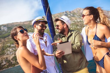 Dijital tablet kullanarak yatta yelken gülümseyen arkadaşlar. Tatil,