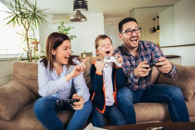 Mutlu aile kanepede oturuyor ve video oyunları oynamak ve yediğine