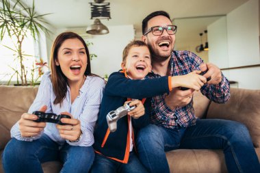 Mutlu aile kanepede oturuyor ve video oyunları oynamak ve yediğine