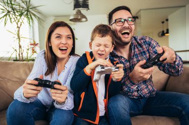Mutlu aile kanepede oturuyor ve video oyunları oynamak ve yediğine