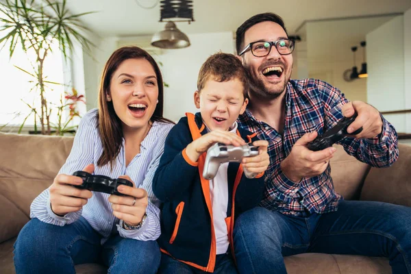 Счастливая семья, сидящая на диване, играющая в видеоигры и кушающая — стоковое фото