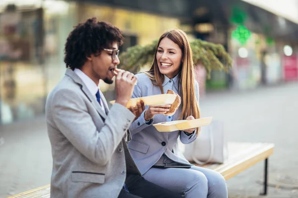 Χαμογελαστοί επιχειρηματίες με σάντουιτς που κάθονται μπροστά από τον υπάλληλο — Φωτογραφία Αρχείου