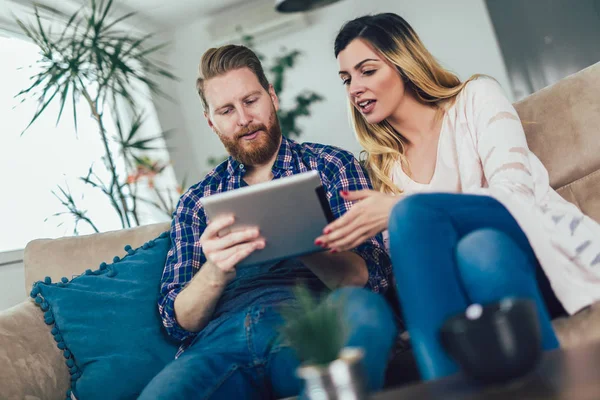 Casal apaixonado sentado no sofá e usando tablet, se divertindo . — Fotografia de Stock