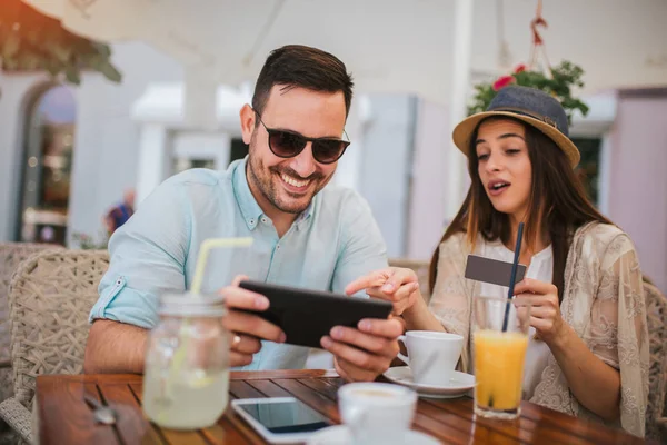 Glückliches junges Paar kauft online ein, während es in einem Café sitzt. — Stockfoto