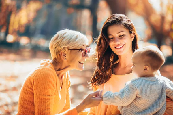 Grandmother and mother smiling at baby in autumn park. — Stock Photo, Image