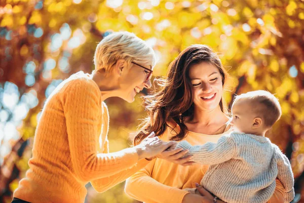 Nonna e madre sorridono al bambino nel parco autunnale . — Foto Stock