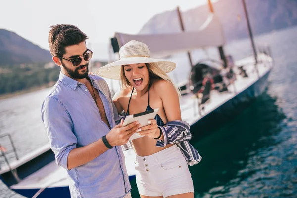 Happy young couple walking by the harbor using digital tablet of — Stock Photo, Image