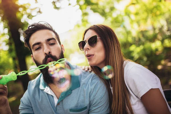 Paar sitzt auf der Parkbank und pustet Suppenblasen auf Bea — Stockfoto