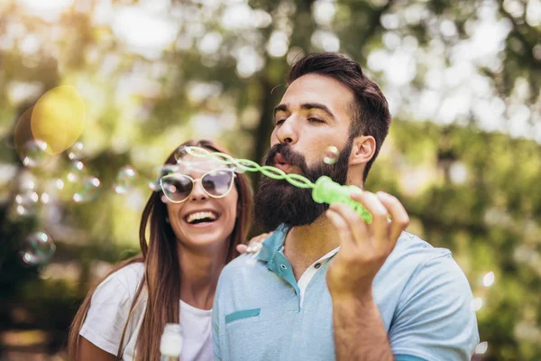 Couple sitting on the park bench and blowing soup bubbles on bea — Stock Photo, Image