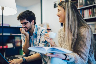 Kafede laptopla çalışan ve gülümseyen genç çift..