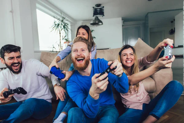 Grupo de amigos juegan videojuegos juntos en casa, divirtiéndose. — Foto de Stock