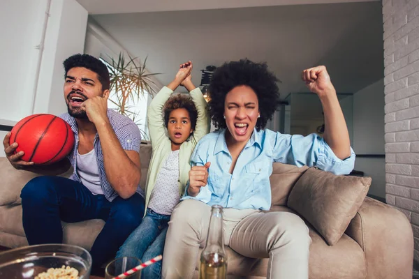 Feliz familia afroamericana de tres viendo la televisión y animando — Foto de Stock