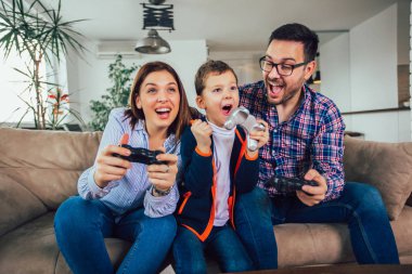Mutlu aile kanepede oturuyor ve video oyunları oynamak ve yediğine