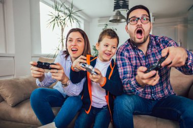Mutlu aile kanepede oturuyor ve video oyunları oynamak ve yediğine